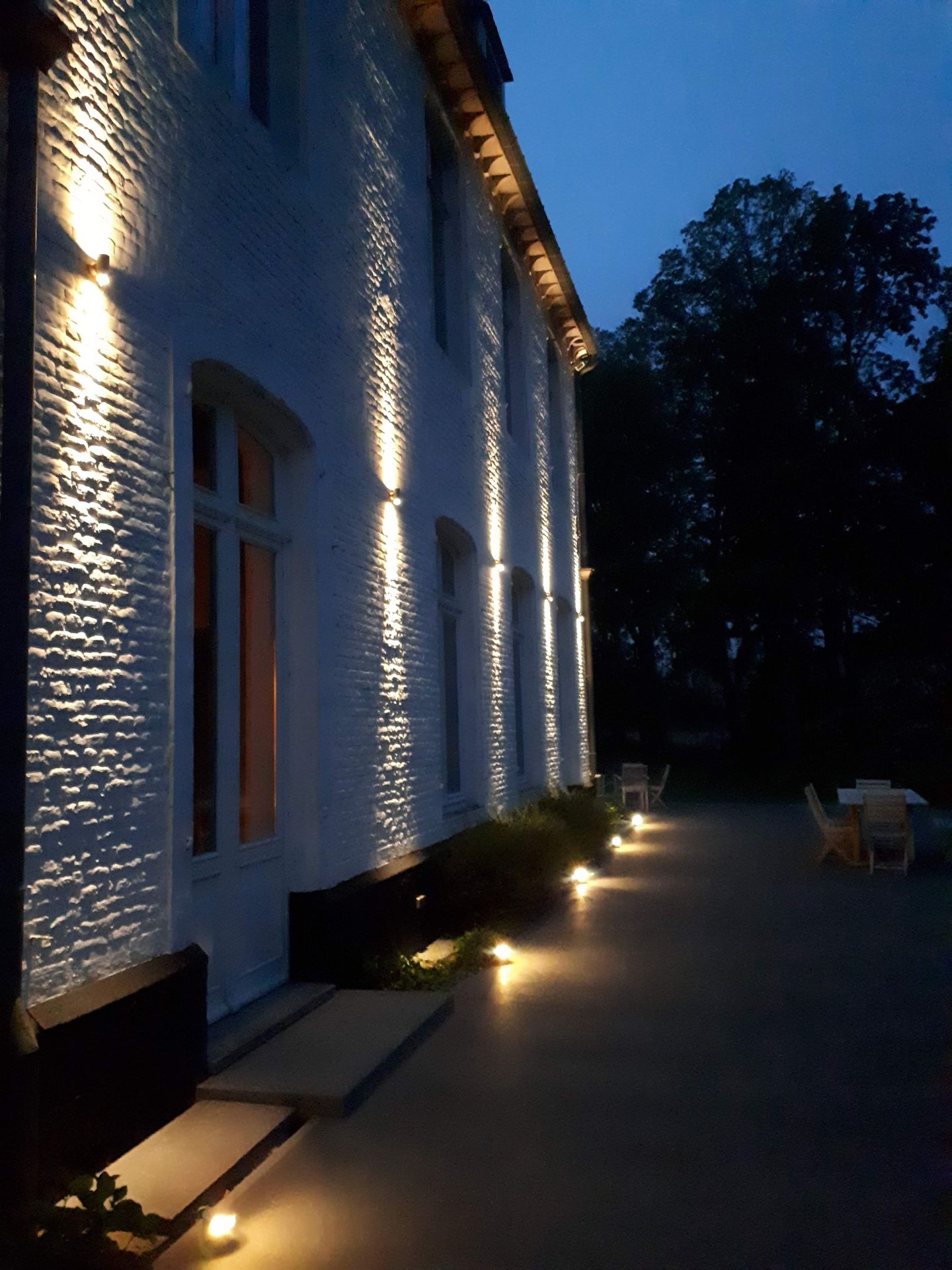 Brass uplights grazing the white wall of a manor house at night